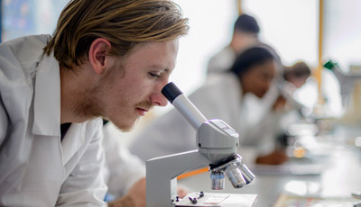 Two students in lab coats looking down a microscope
