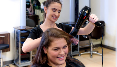 Student hairdresser chatting to a client as she blowdrys her hair
